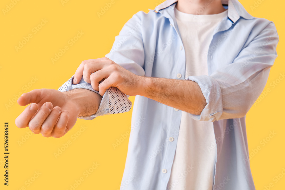 Young man rolling up his sleeve on yellow background, closeup