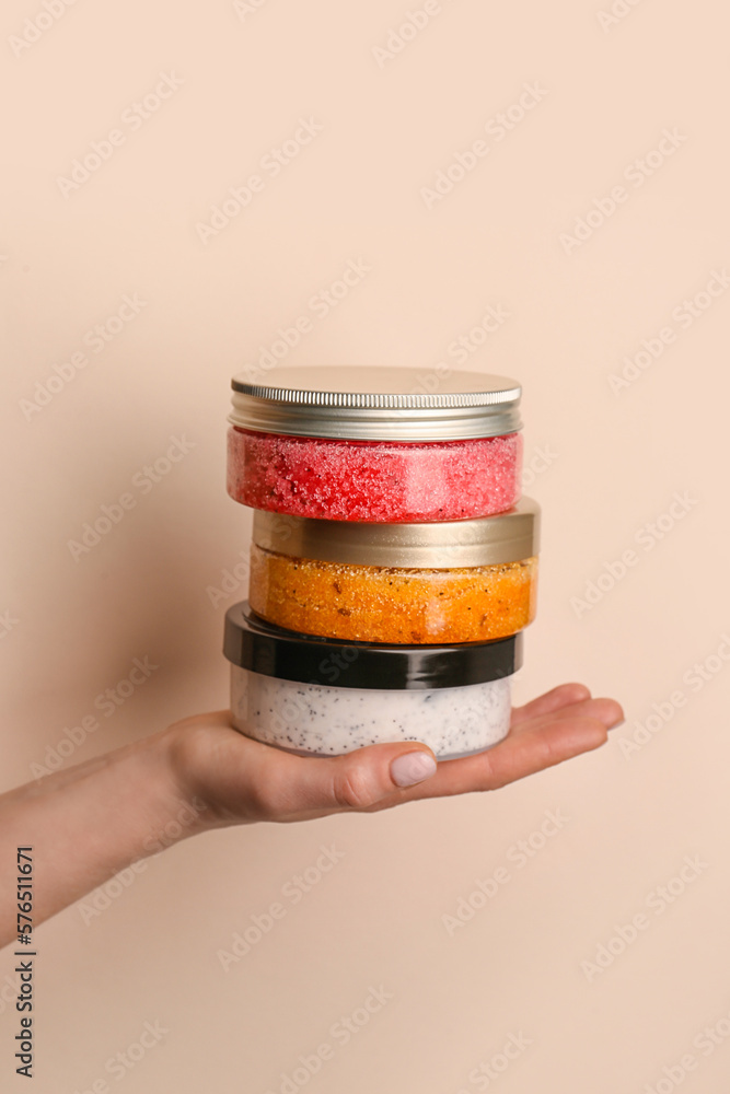 Female hand with jars of natural body scrub on color background, closeup