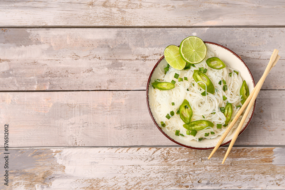 Bowl of tasty rice noodles with chili pepper and lime on light wooden background