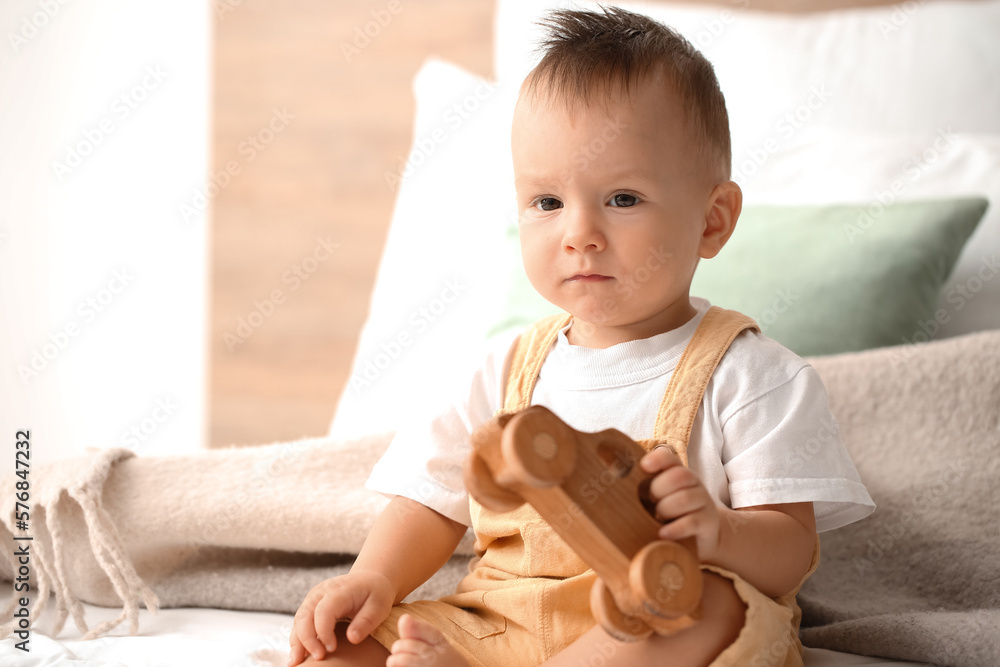 Baby boy playing with wooden car in bedroom, closeup