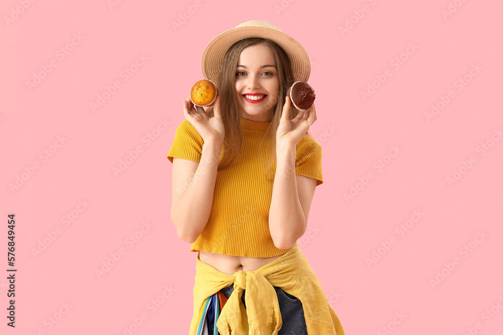 Young woman in hat with tasty muffins on pink background