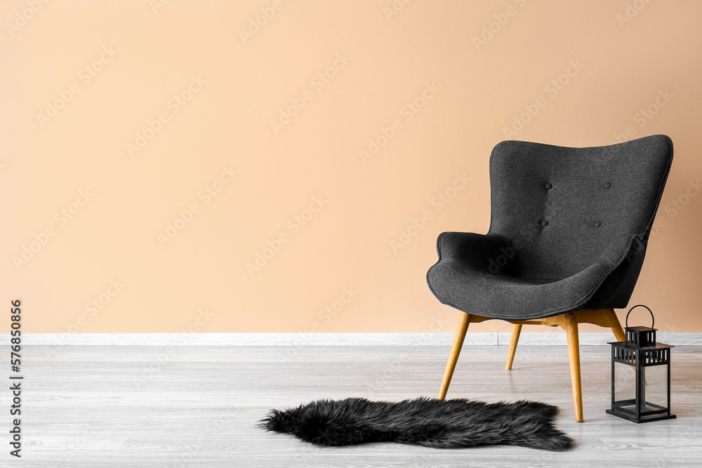 Stylish grey armchair, lantern and black fur rug near beige wall