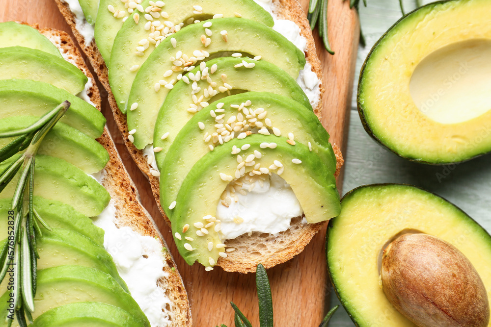 Board with delicious avocado toasts and rosemary on green wooden background, closeup