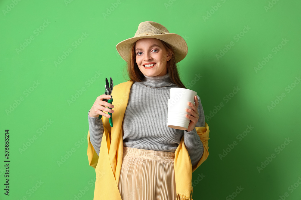 Young woman with pruner and pots for plants on green background