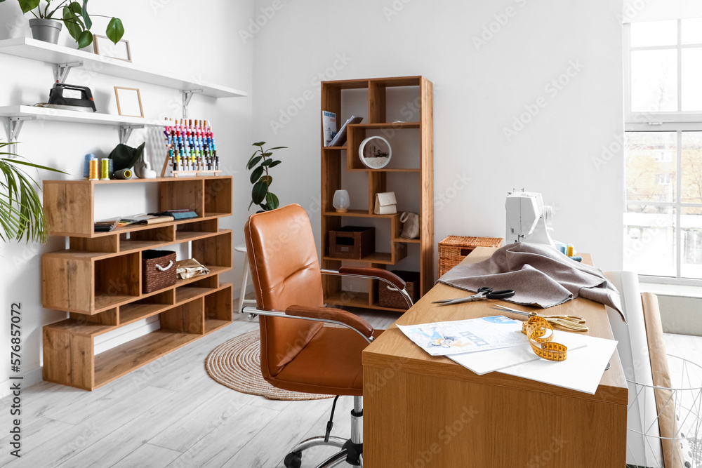 Interior of modern atelier with tailors workplace and shelving units