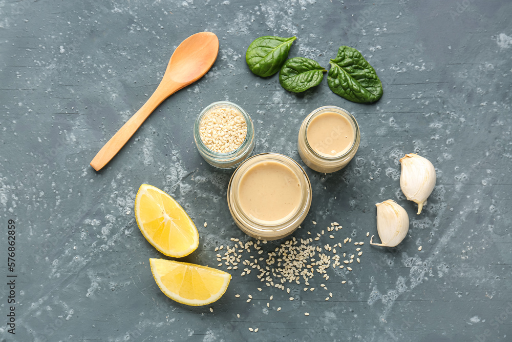 Composition with tasty tahini, sesame seeds, garlic, spinach and lemon slices on dark background