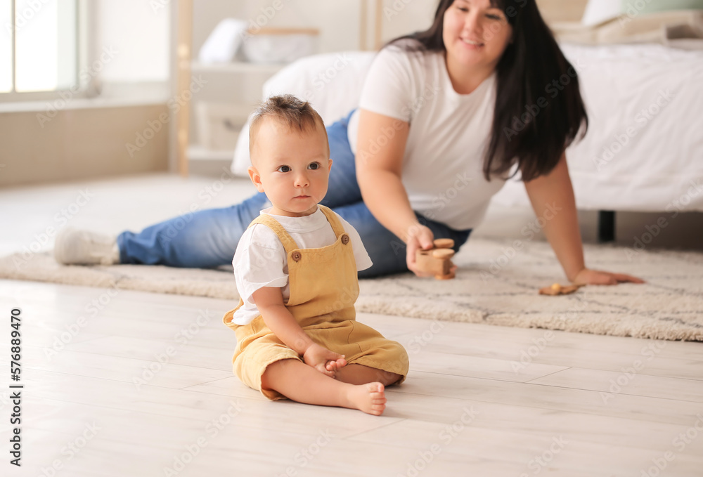 Cute baby boy sitting on floor in bedroom