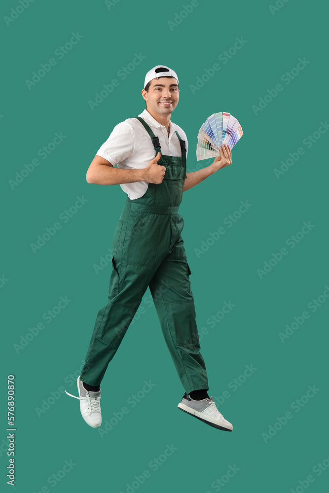 Male painter with color palettes jumping on green background