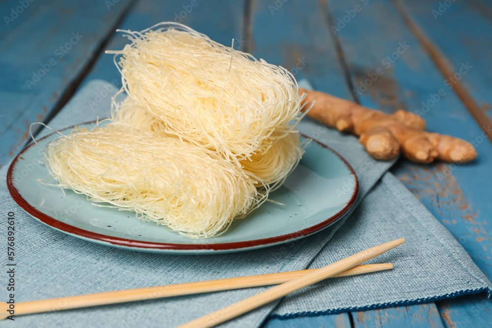 Plate of raw rice noodles and chopsticks on color wooden background