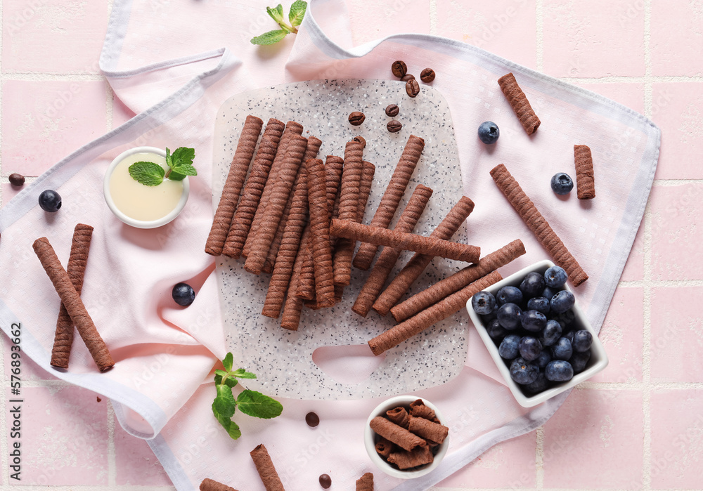 Board with delicious chocolate wafer rolls, blueberries, condensed milk and coffee beans on pink til