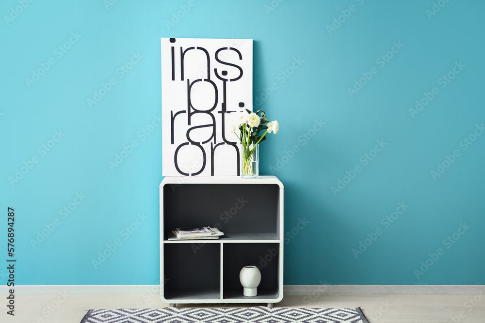 Vase with ranunculus flowers and poster on shelf near blue wall in room