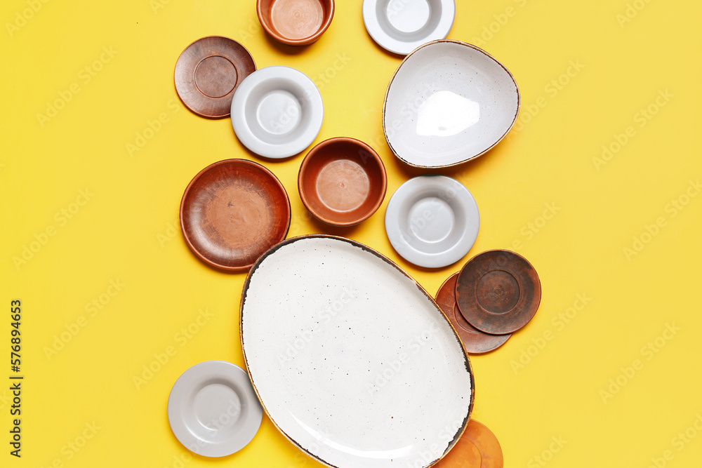 Composition with clean ceramic plates and bowls on yellow background