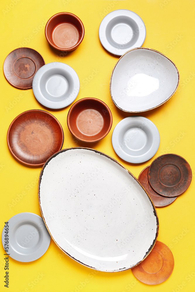 Composition with clean ceramic plates and bowls on yellow background