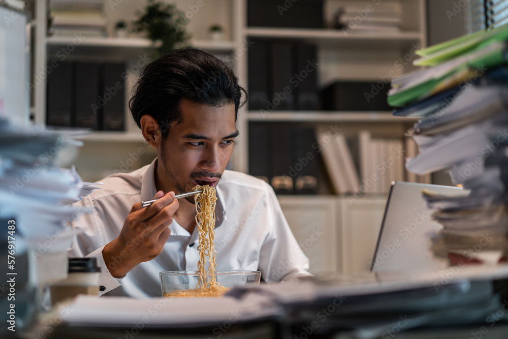 Asian young businessman eating noodles while working in office at night. 