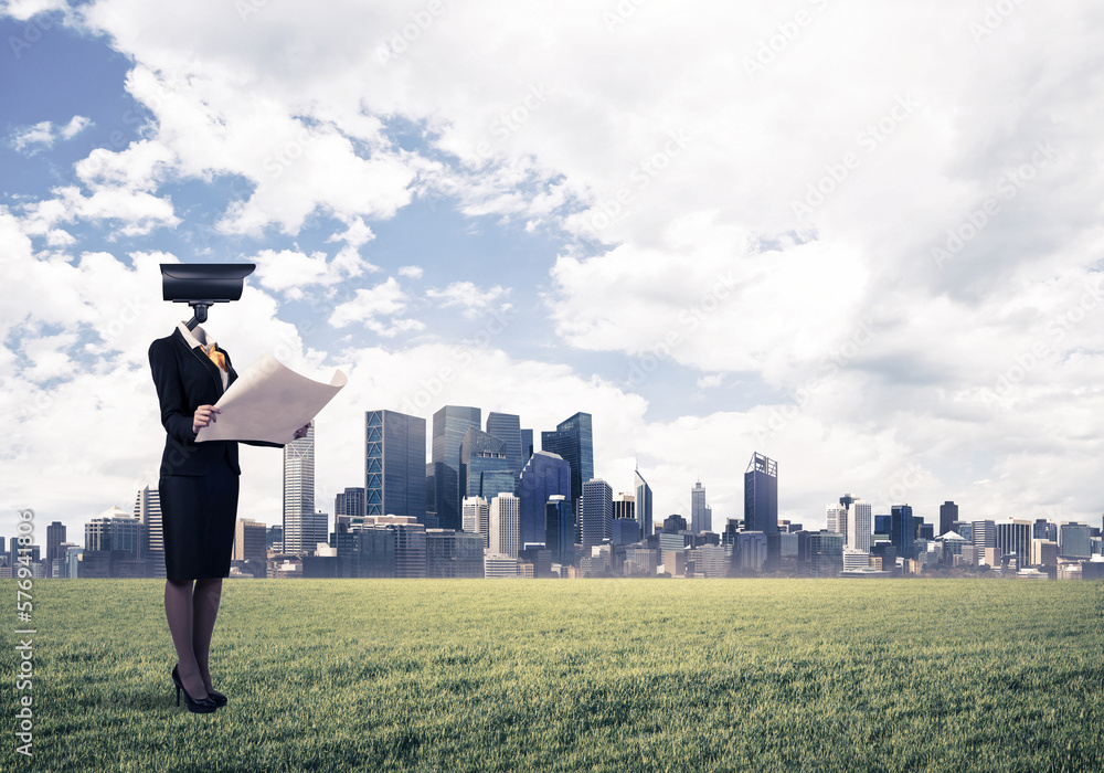 Camera headed woman standing on green grass against modern cityscape