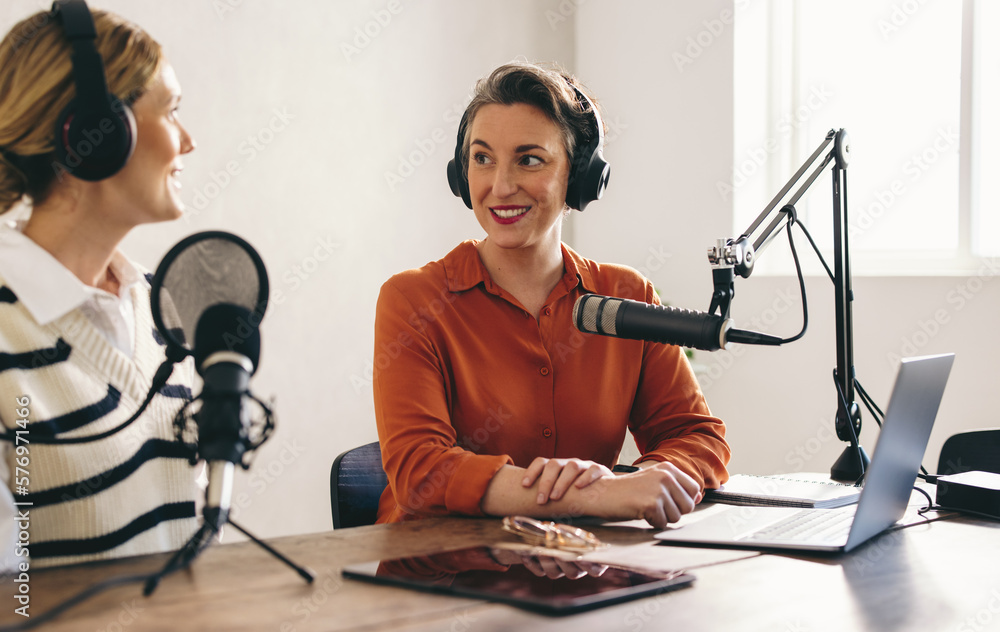 Two happy women co-hosting a podcast in a home studio