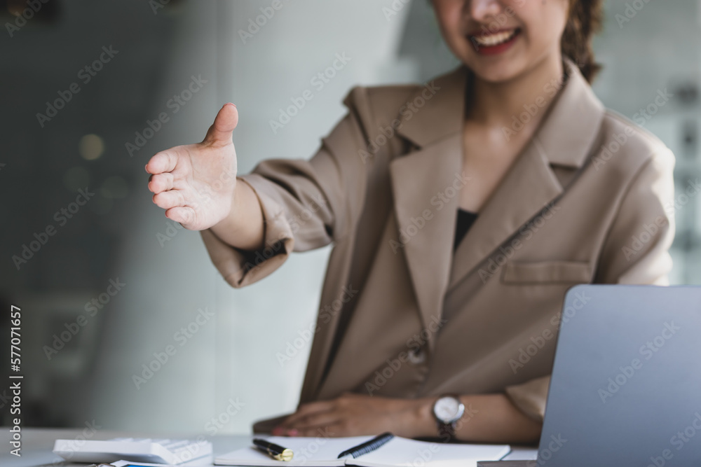 Charming Asian businesswoman in office looking smiling and shaking hands.