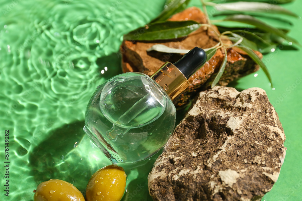 Composition with bottle of olive essential oil and stones in water on color background, closeup