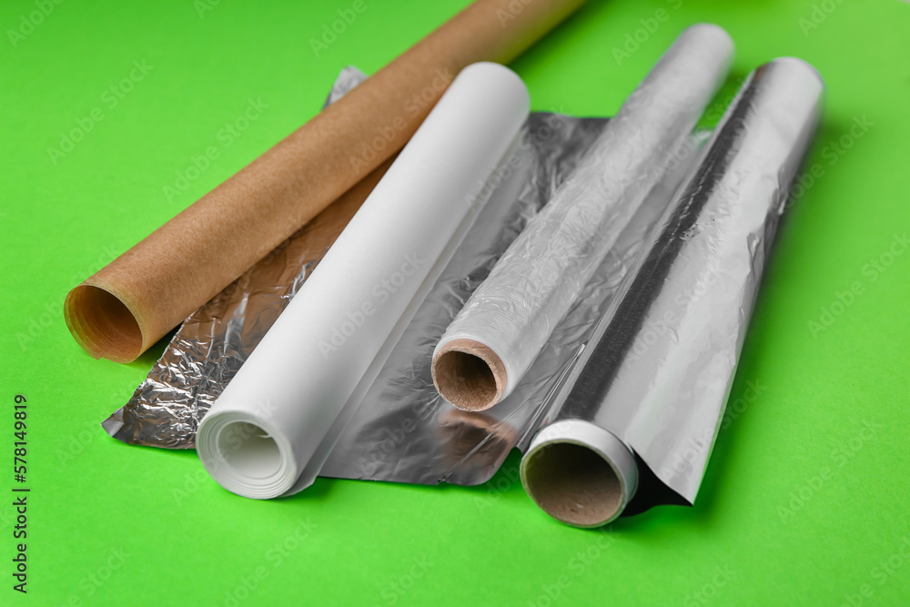 Rolls of aluminium foil, baking paper and food film on green background, closeup