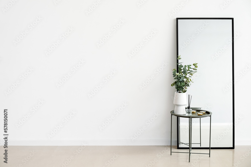 Vase with eucalyptus, reed diffuser and candles on table near mirror in light room