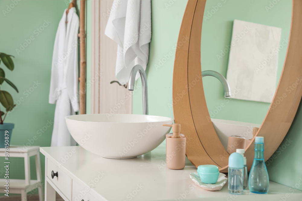 Interior of bathroom with ceramic sink and bath accessories near mirror