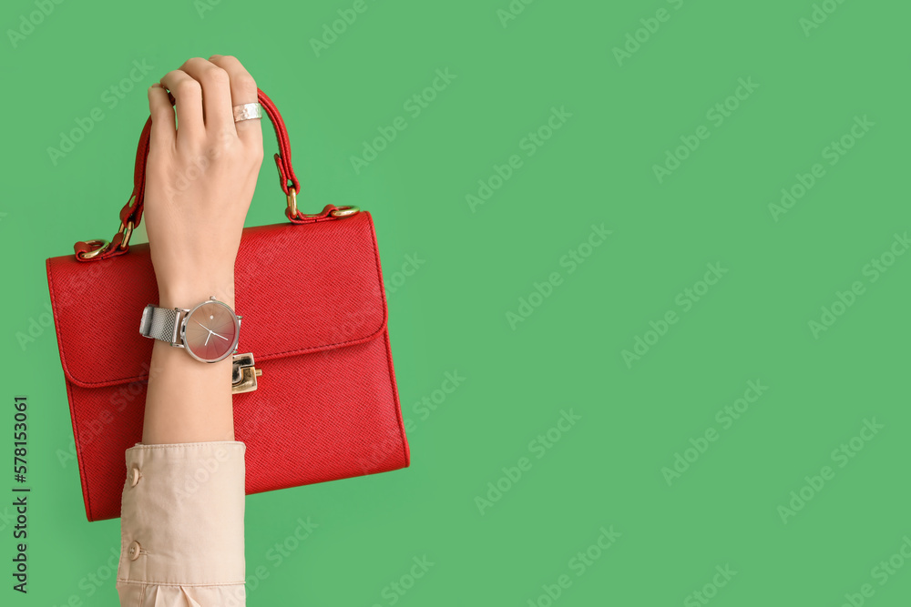 Woman with stylish wristwatch and bag on green background