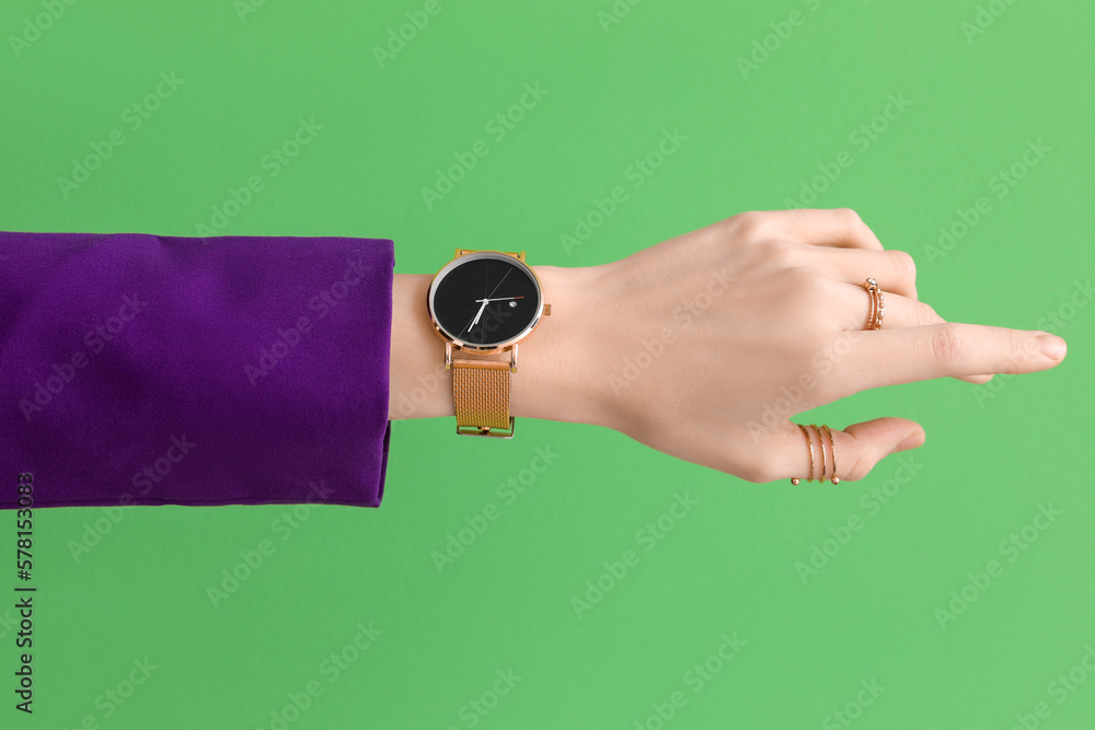 Woman with golden wristwatch on green background