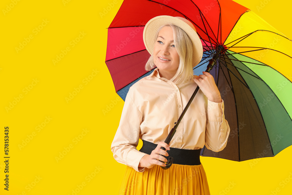 Beautiful mature woman with rainbow umbrella on yellow background