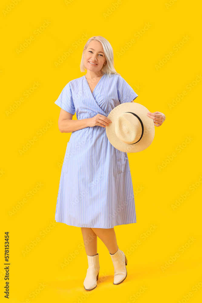 Stylish blonde mature woman with hat on yellow background