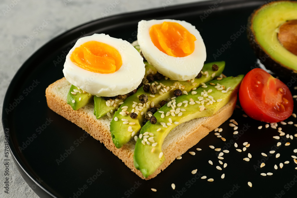 Delicious avocado toast with boiled egg on black plate, closeup