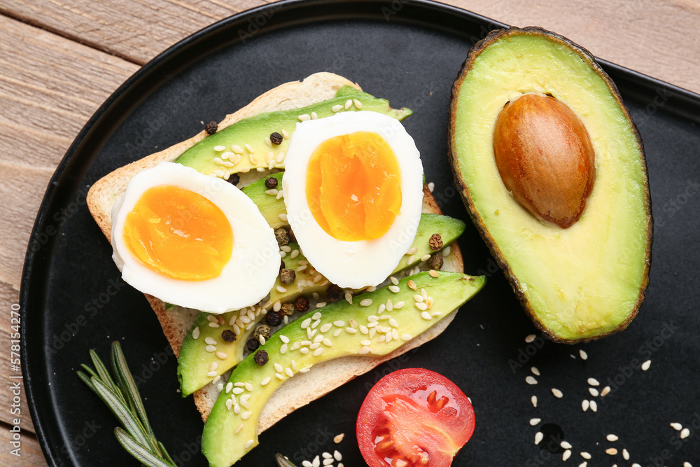 Delicious avocado toast with boiled egg on black plate, closeup