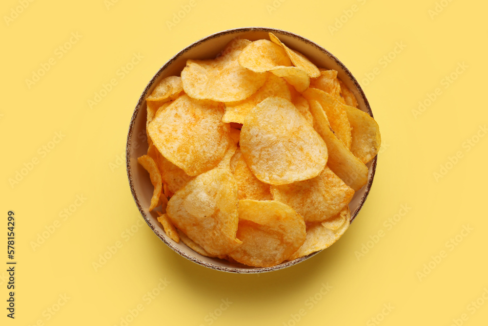 Bowl with delicious potato chips on yellow background