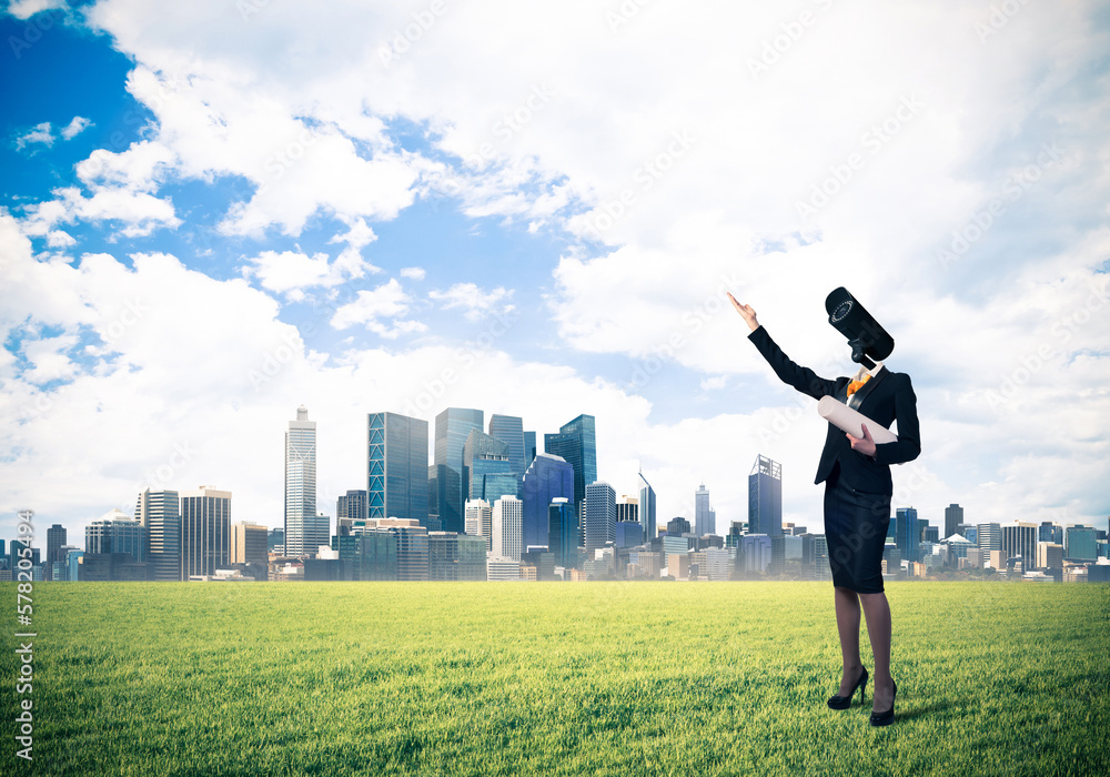 Camera headed woman standing on green grass against modern cityscape