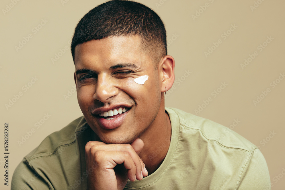 Fun skincare routine: Handsome young man smiles with beauty cream on his face