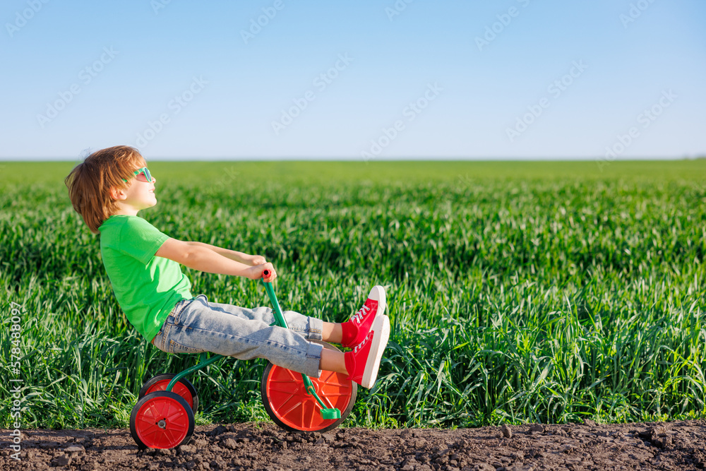 Happy child riding bike outdoor in spring green field