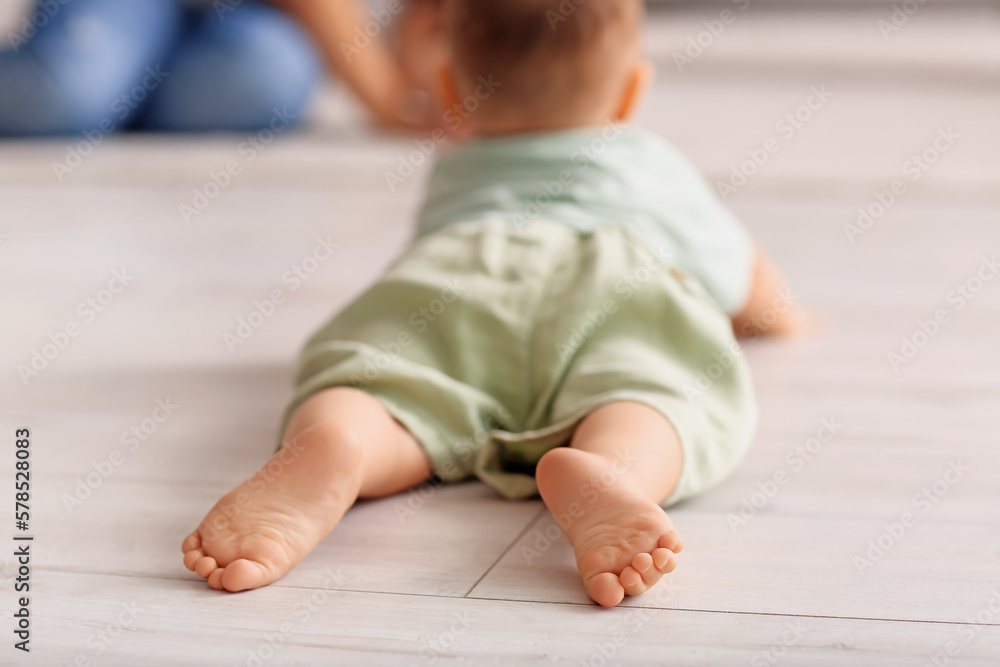 Small feet of baby boy lying on floor at home, closeup