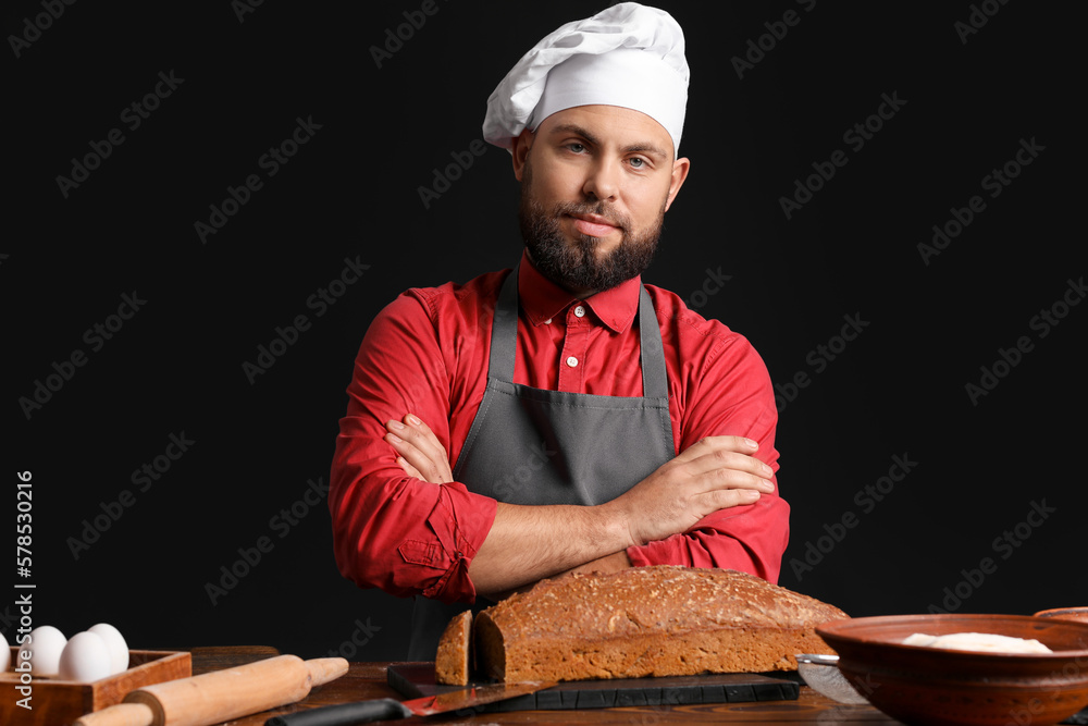 Male baker at table with rye bread on dark background