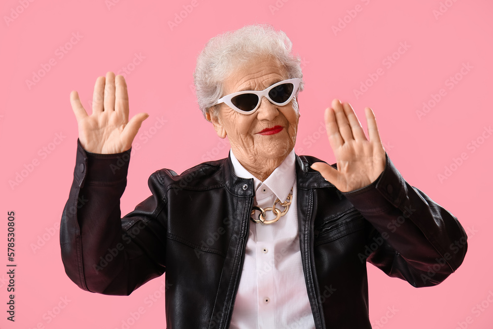 Senior woman in sunglasses showing hands on pink background