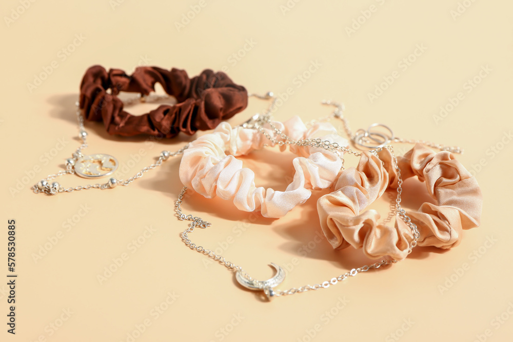 Silk scrunchies and necklaces on color background