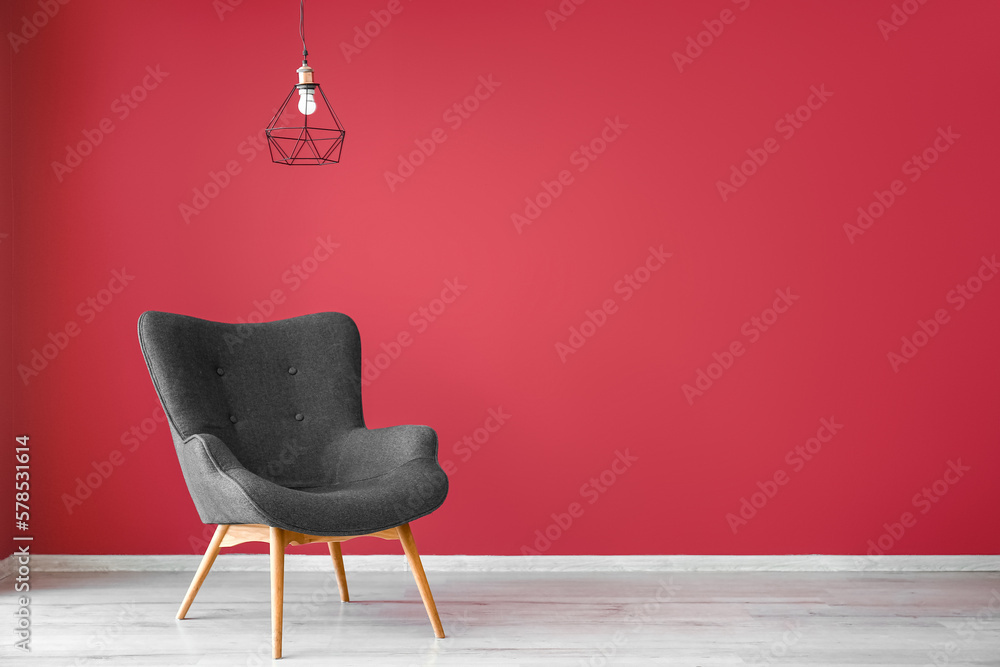 Stylish grey armchair and lamp near red wall