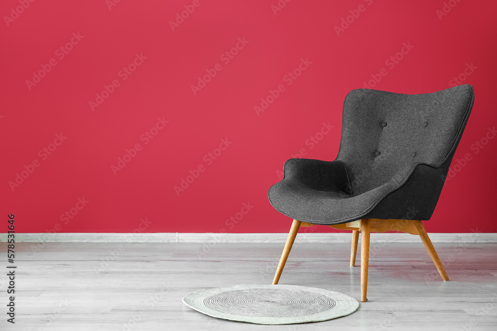 Stylish grey armchair and wicker rug near red wall