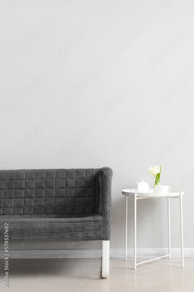 Stylish grey sofa and table near white wall