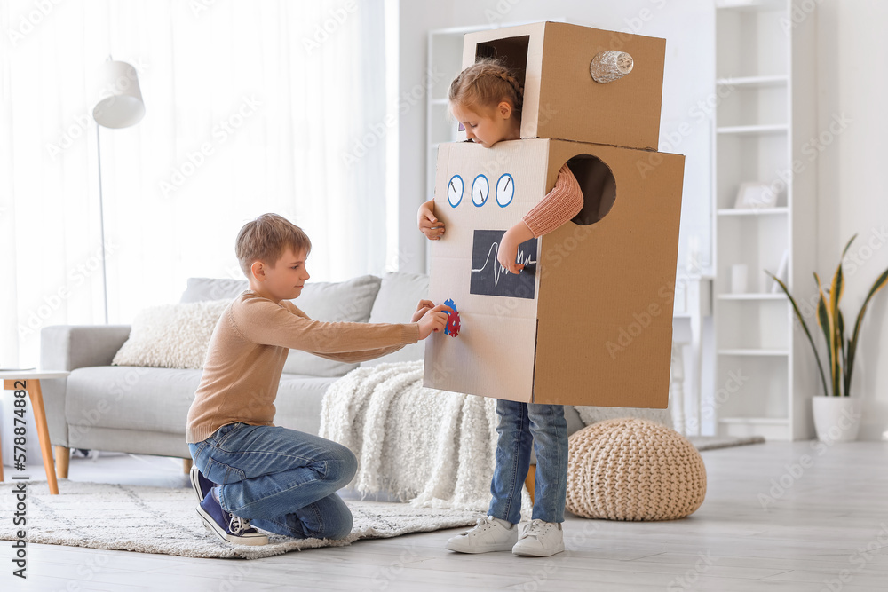 Little girl in cardboard robot costume playing with her brother at home