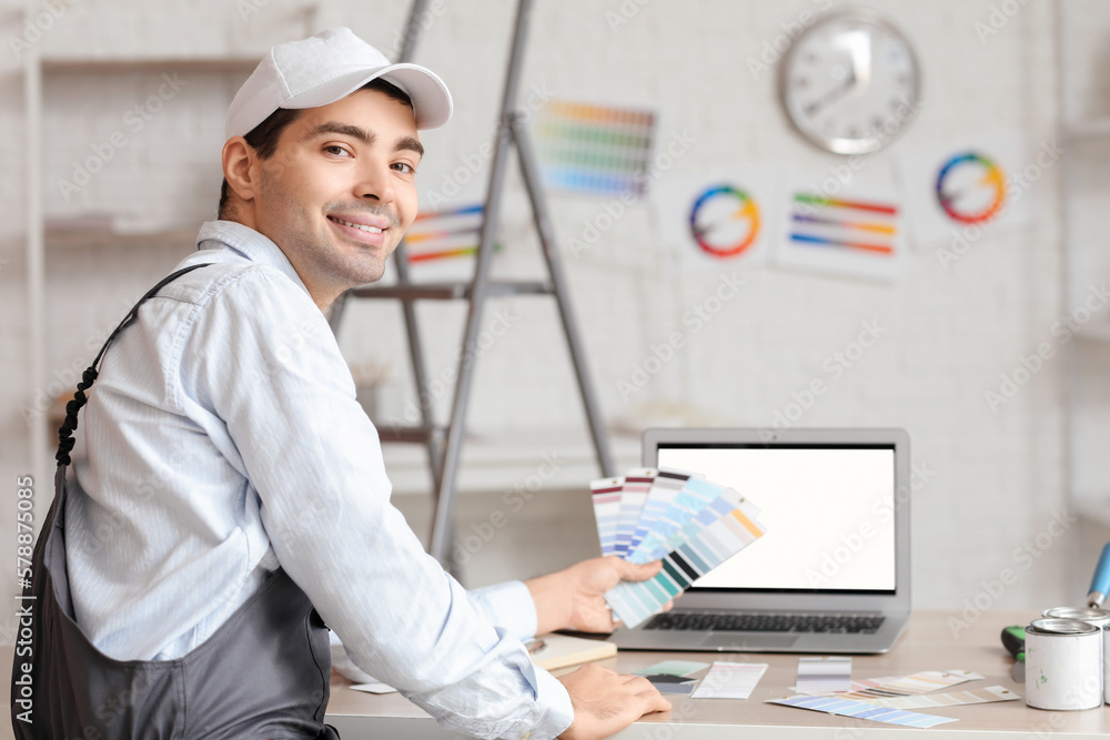 Male painter with color palettes sitting at table in room