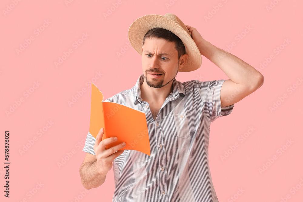 Confused young man in straw hat with copybook on pink background