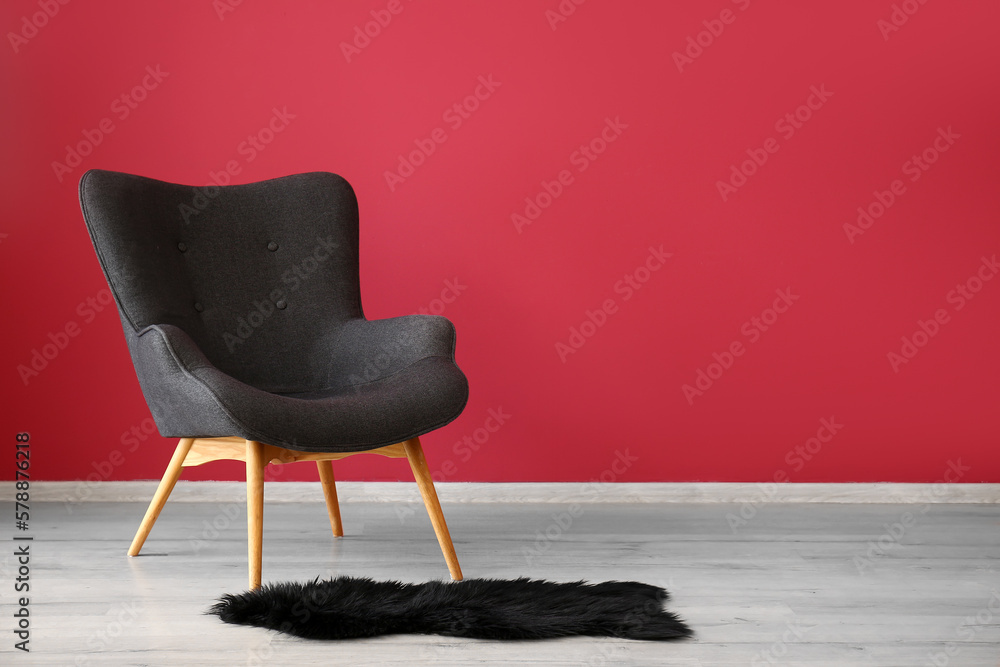 Stylish grey armchair and black fur rug near red wall