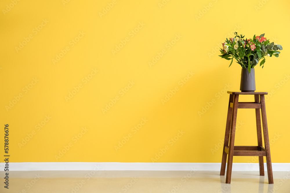 Vase with beautiful alstroemeria flowers on stool near yellow wall