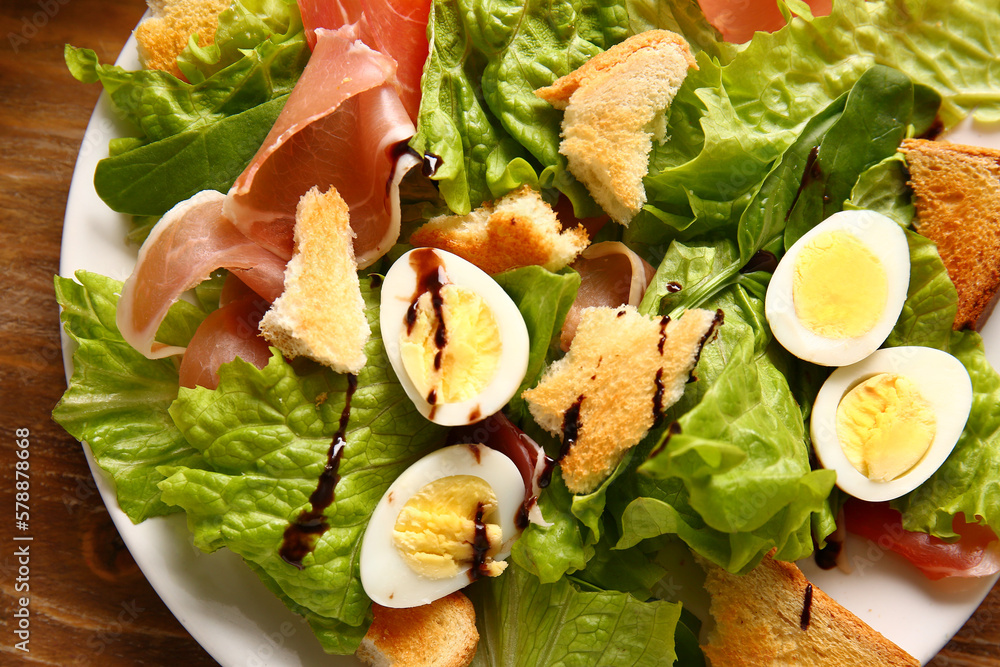 Plate of delicious salad with boiled eggs and jamon on brown wooden background