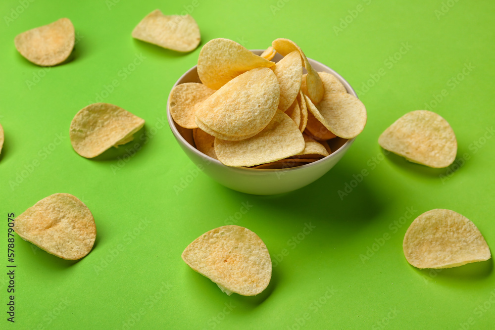 Bowl with delicious potato chips on green background