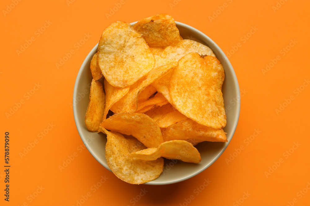 Bowl with delicious potato chips on orange background